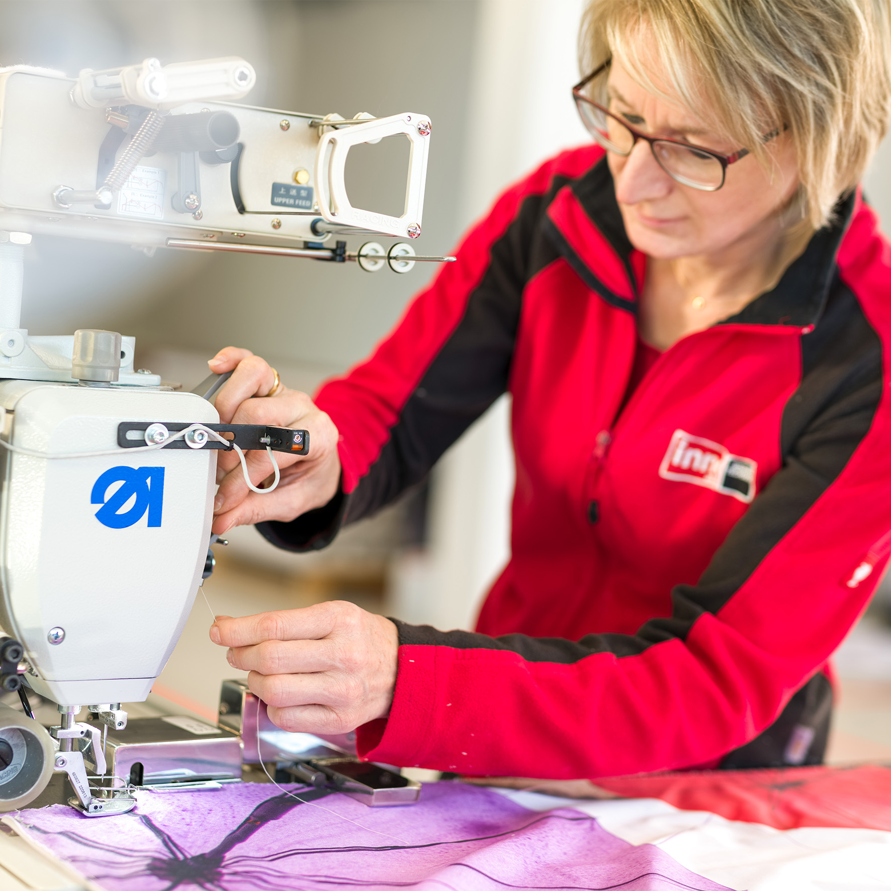 Mitarbeiterin beim Nähen eines Flachkeders an einen Textildruck